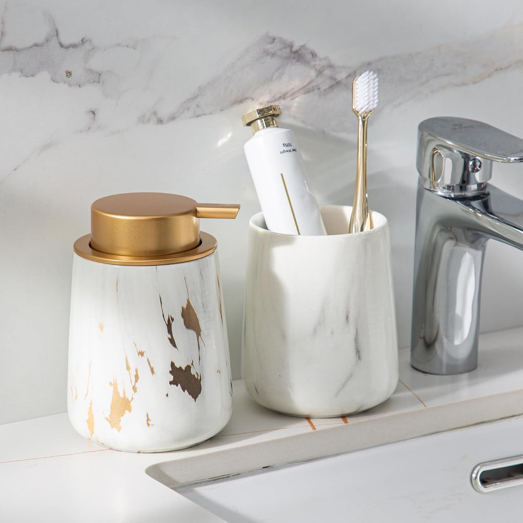 Gold-accent ceramic soap dispenser at a bathroom sink beside a toothbrush cup