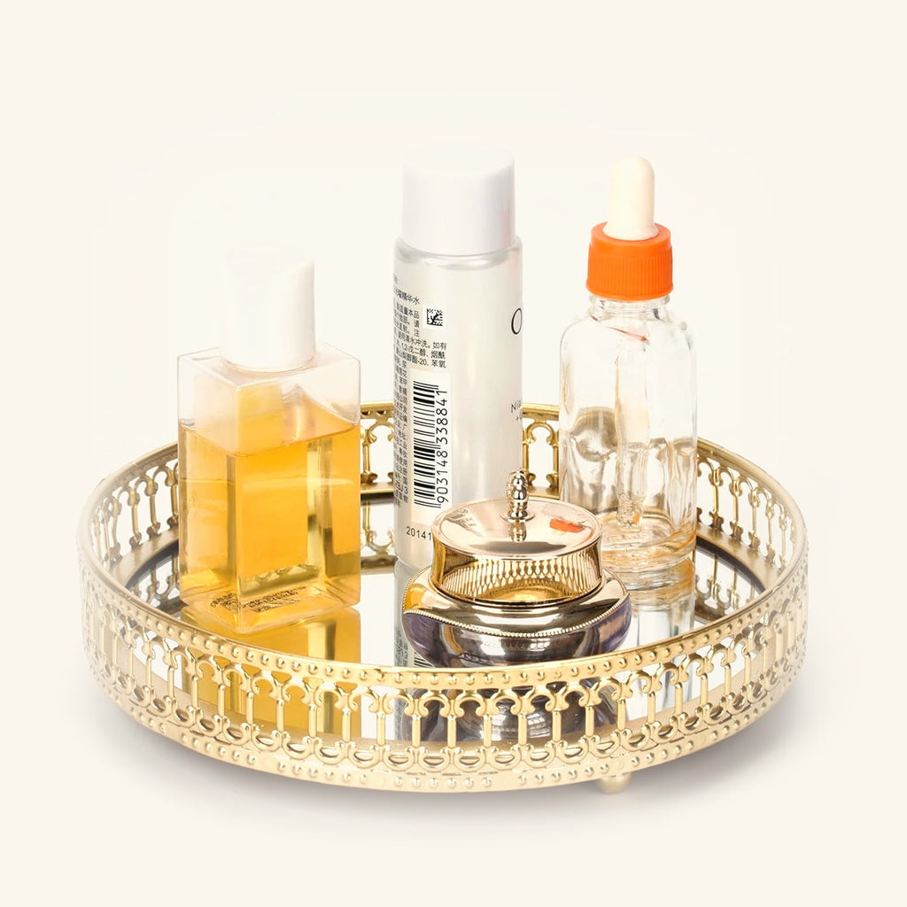 Small round gold mirrored vanity tray holding perfume and skincare bottles
