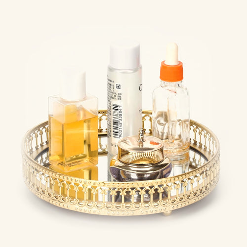 Small round gold mirrored vanity tray holding perfume and skincare bottles